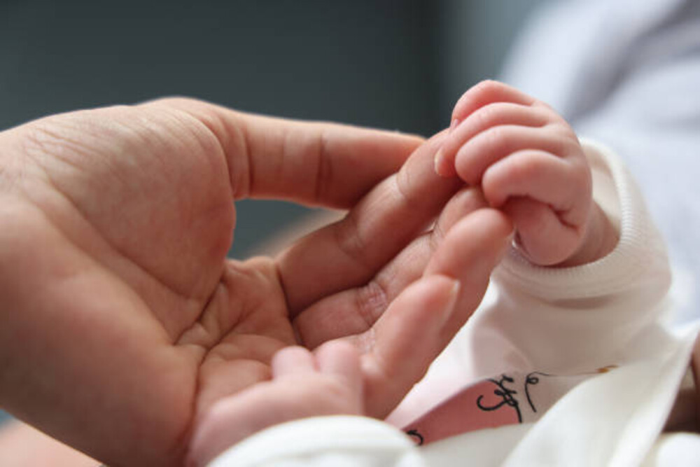A representational image showing an adult gently holding the hand of a newborn baby.
