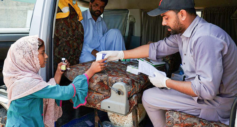 A healthcare worker in Pakistan hands medicine to a young girl at a mobile clinic in a flood-affected area.