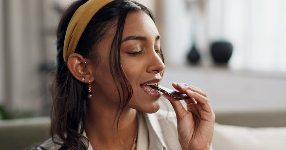 A woman enjoying chocolate, illustrating premenstrual cravings and the desire for sweet foods during PMS.