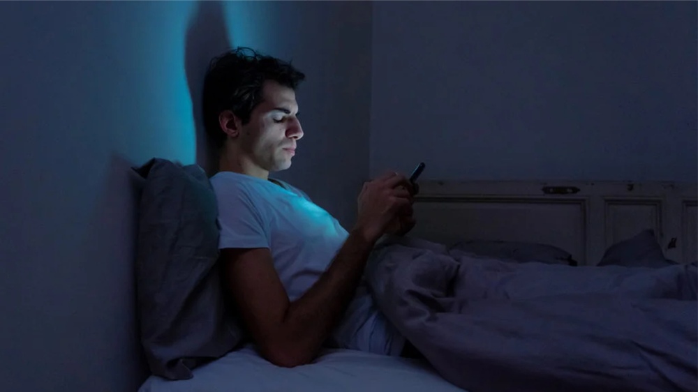 A young person using social media late at night under dim light, reflecting the impact on mental health