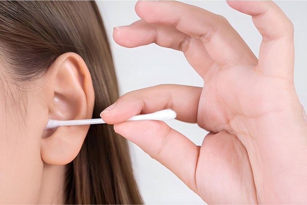 A woman carefully cleaning her ears with a cotton bud, highlighting safe ear hygiene practices