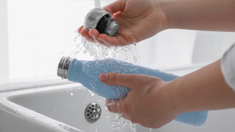 Professional cleaning of a reusable water bottle with warm soapy water and a bottle brush for hygiene and safety