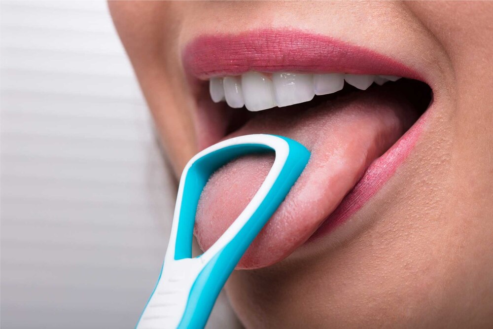 A woman using a tongue scraper to clean her tongue for better oral hygiene and fresh breath