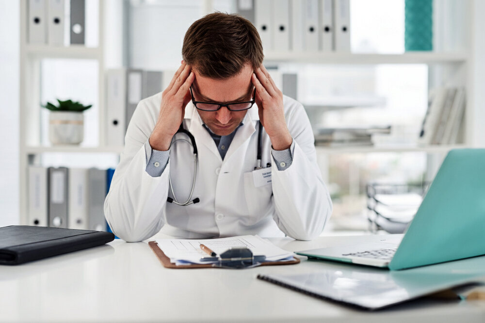 A doctor sitting with head in hands, showing burnout, mental stress, and healthcare pressure
