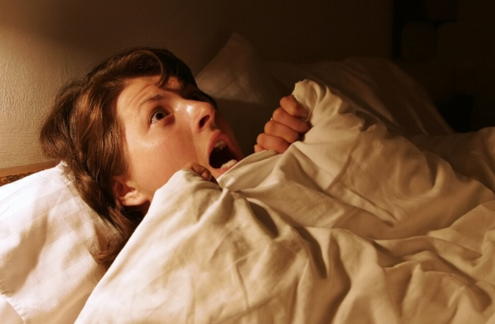A woman lying in bed, awake and distressed, experiencing a vivid nightmare at night, showing stress and fear