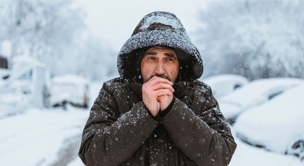 A young man shivering in extreme cold weather, illustrating hypothermia risk and winter safety