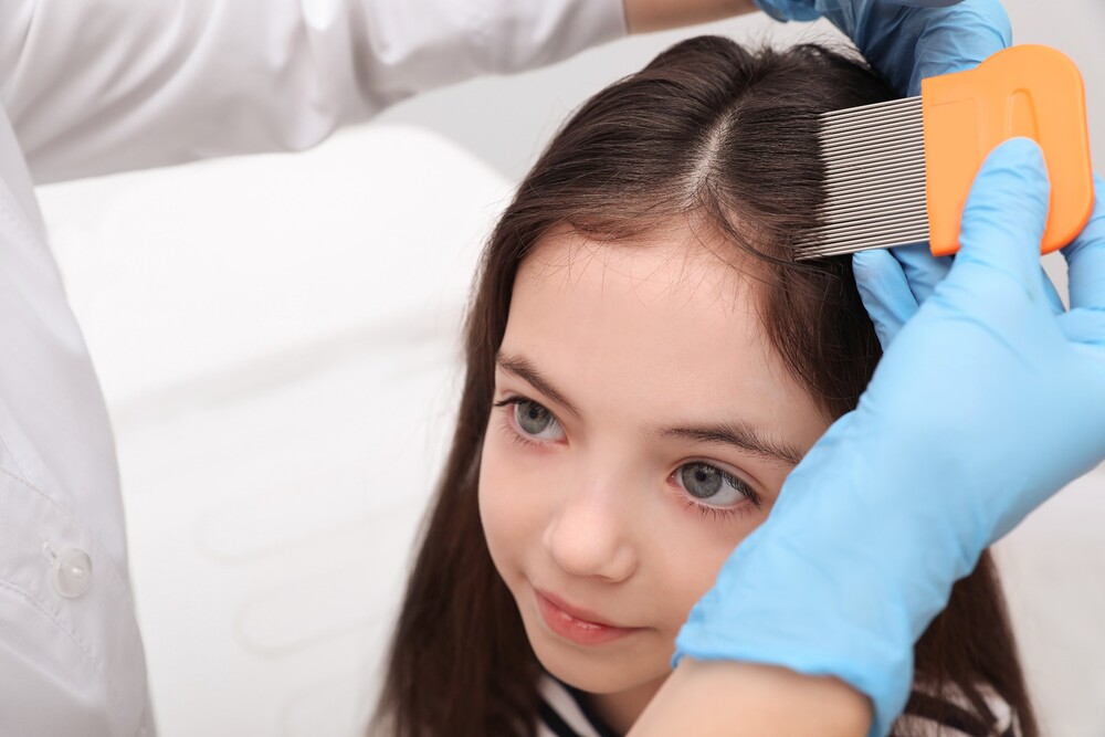 A caregiver carefully combs a baby girl's hair while checking for body lice