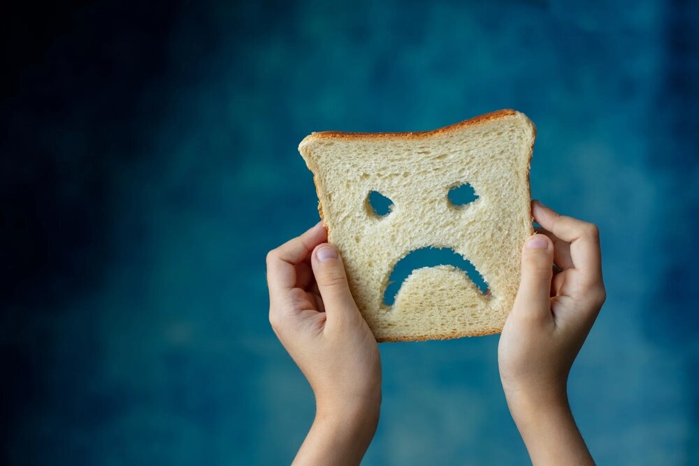 Woman holding a slice of bread with a sad face drawn on it, symbolizing celiac disease