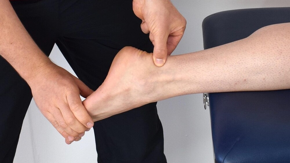 Orthopedic surgeon examining a patient with an Achilles tendon rupture, assessing the back of the ankle and heel for pain, swelling, and tendon injury