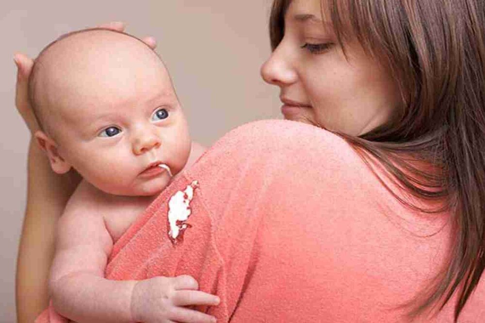 Baby spitting up milk on mother's shoulder after feeding due to infant reflux