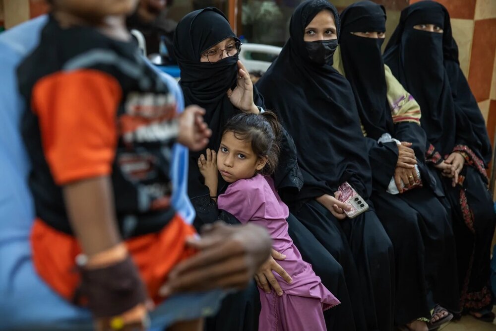 Women and children seated together, accompanying a report on financial aid for mothers of children with HIV in Sindh