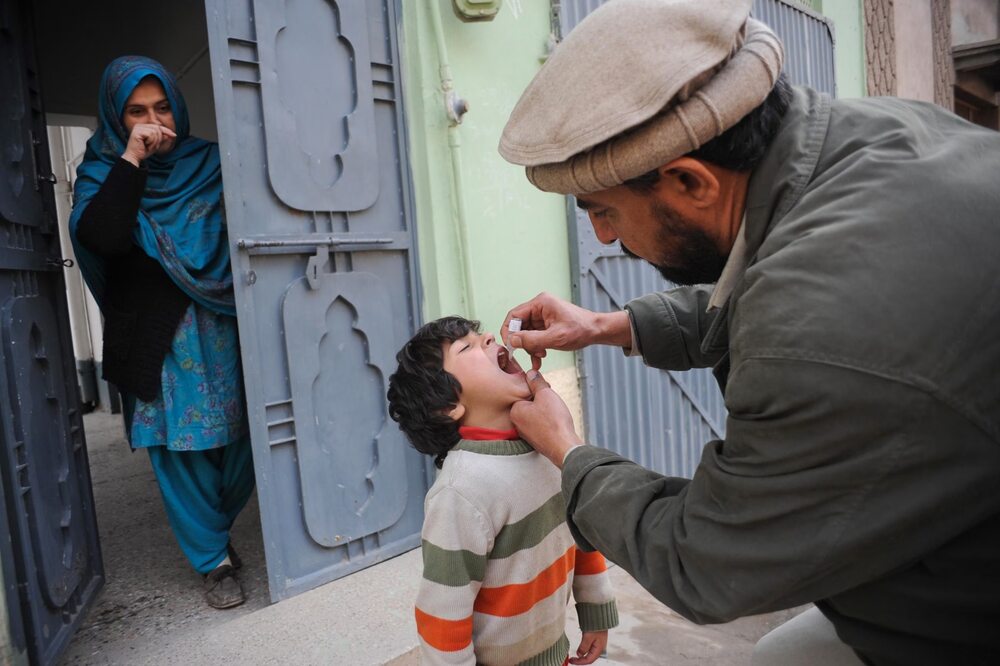 Health worker giving oral polio vaccine drops to a child at a doorstep in Pakistan as part of efforts to expand childhood vaccination coverage.