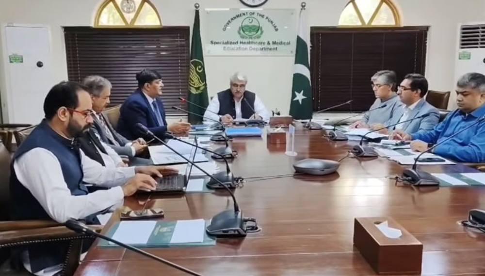 : A formal board meeting at the Punjab Health Initiative Management Company, with the health minister and officials seated around a conference table reviewing healthcare reports and financial documents, symbolizing the presentation of free treatment details.